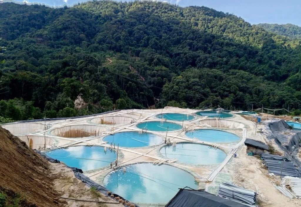 Aerial view of industrial rare earth mining ponds in a lush, mountainous region of Myanmar.