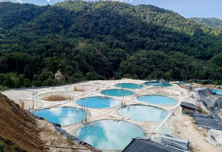 Aerial view of industrial rare earth mining ponds in a lush, mountainous region of Myanmar.
