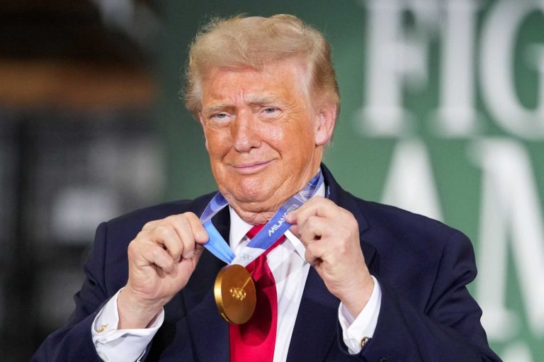 Donald Trump smiling while holding a gold medal around his neck.