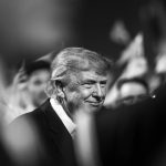 A black and white portrait of Donald Trump smiling among a crowd.