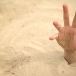 A human hand emerging from deep sand, reaching upward.