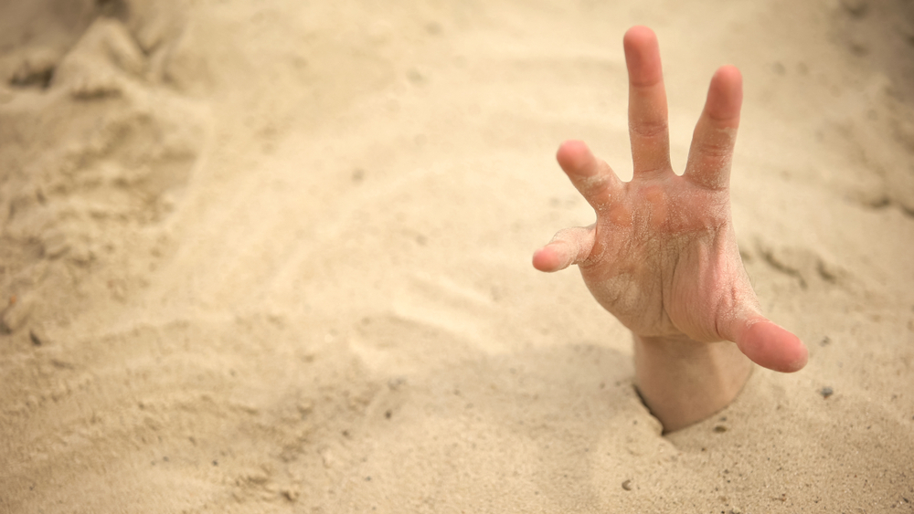 A human hand emerging from deep sand, reaching upward.