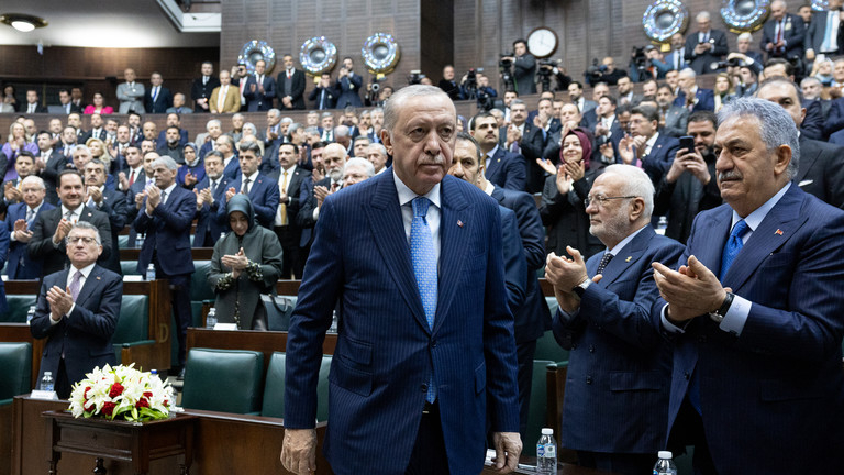 Turkish President Recep Tayyip Erdoğan walking through a crowded assembly hall.