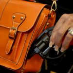 A person removing a handgun from an orange purse.