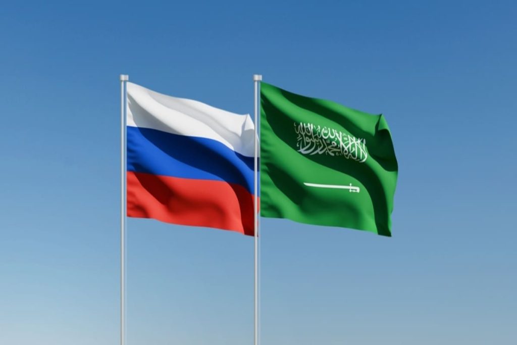 The national flags of Russia and Saudi Arabia waving against a clear blue sky.