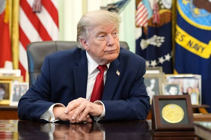 Former President Donald Trump seated at a desk while speaking.