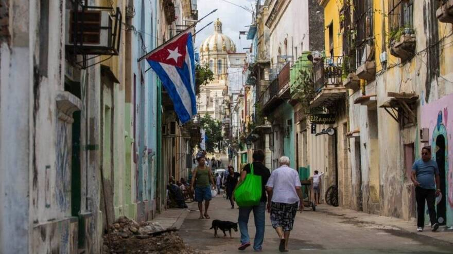 People walking down a narrow street in Havana with a Cuban flag hanging from a building.