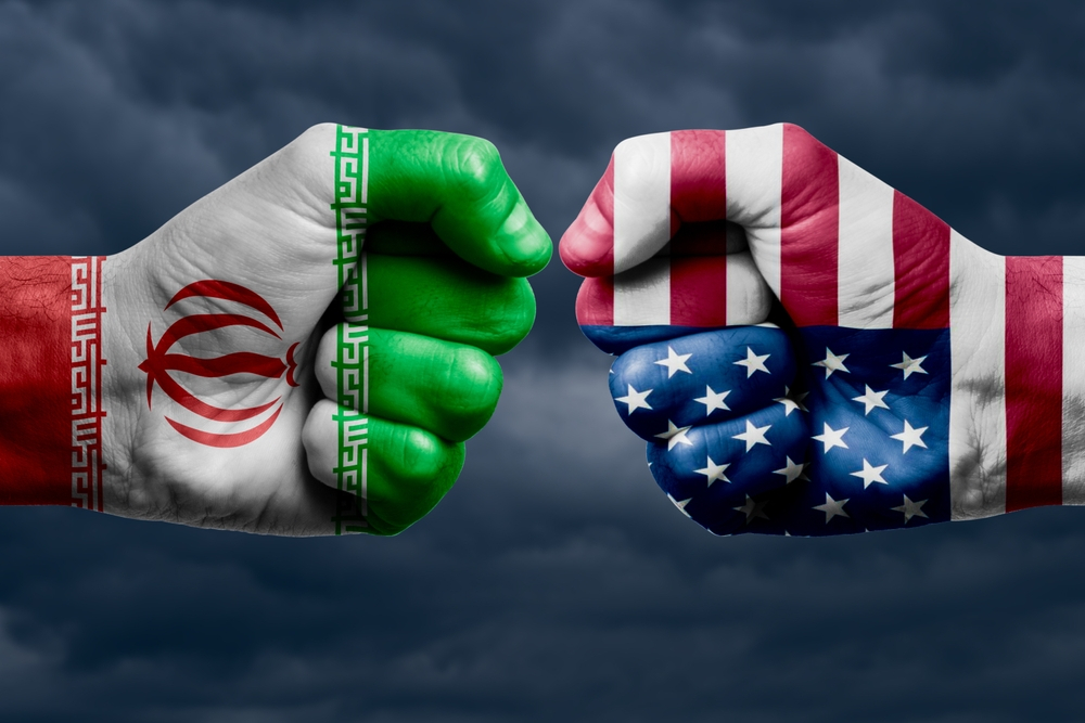 Conceptual image of two giant fists bumping, one painted with the Iranian flag and the other with the US flag, against a stormy sky.