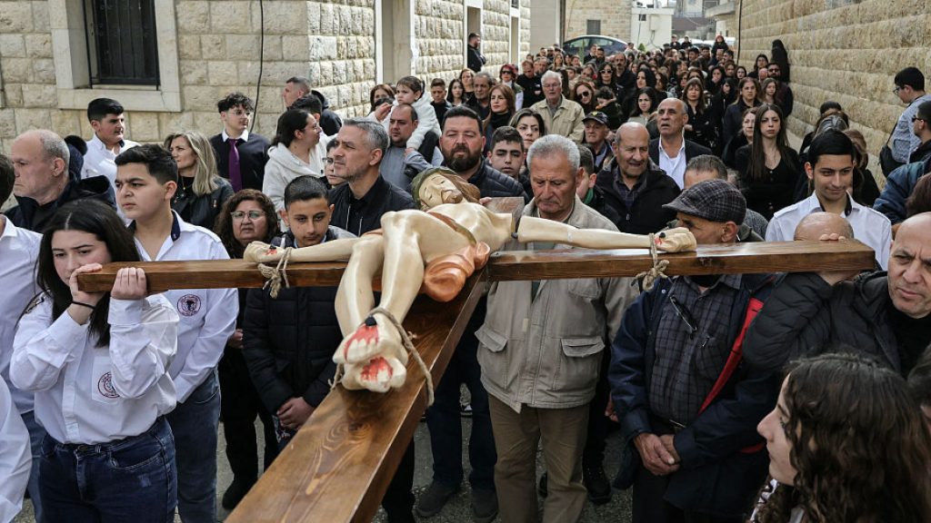 A group of people carrying a large wooden crucifix through a crowded street during a religious procession.