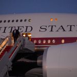 People descending the stairs of a United States government aircraft at twilight.