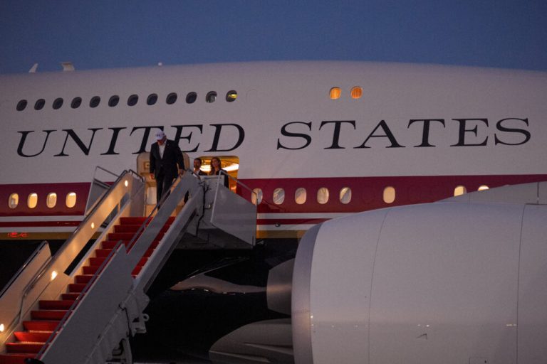 People descending the stairs of a United States government aircraft at twilight.