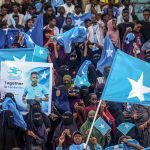 A large crowd of spectators waving Somali flags in a stadium during a public event.