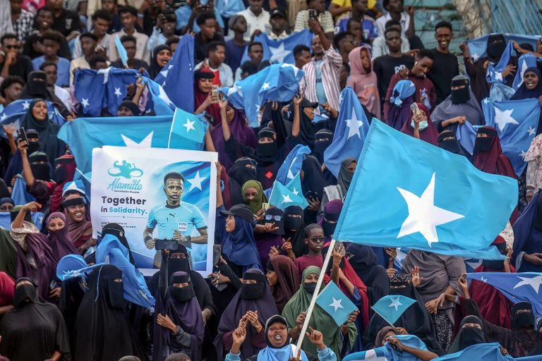 A large crowd of spectators waving Somali flags in a stadium during a public event.