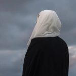 A person wearing a hijab looking out over a cloudy sky.