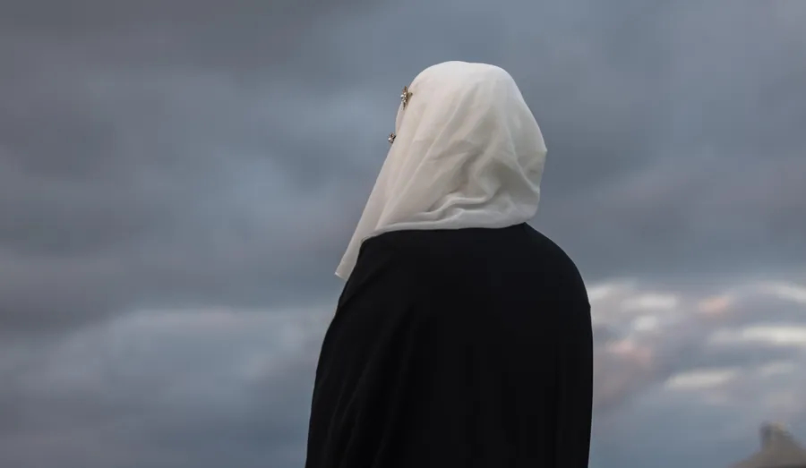 A person wearing a hijab looking out over a cloudy sky.