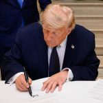 Donald Trump signing an official document at a desk.