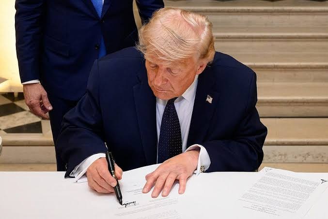 Donald Trump signing an official document at a desk.