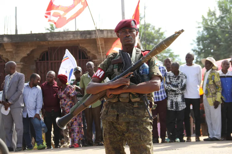 A soldier in camouflage uniform holding a rocket-propelled grenade launcher in a public setting.