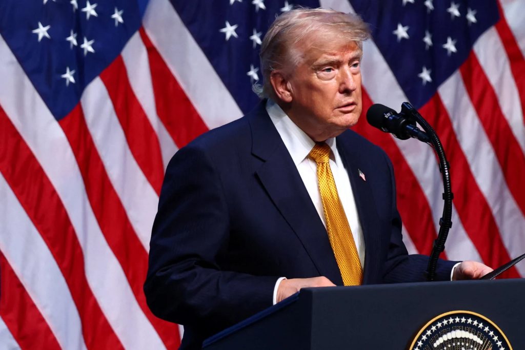Former President Donald Trump speaking at a podium with American flags in the background.