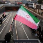 A person waving the Iranian flag over a highway.