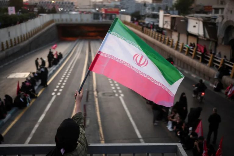 A person waving the Iranian flag over a highway.