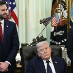 Donald Trump sits at a desk in the Oval Office flanked by two other men in suits.