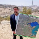 Bezalel Smotrich holding a large map of the E1 area near Jerusalem outdoors.