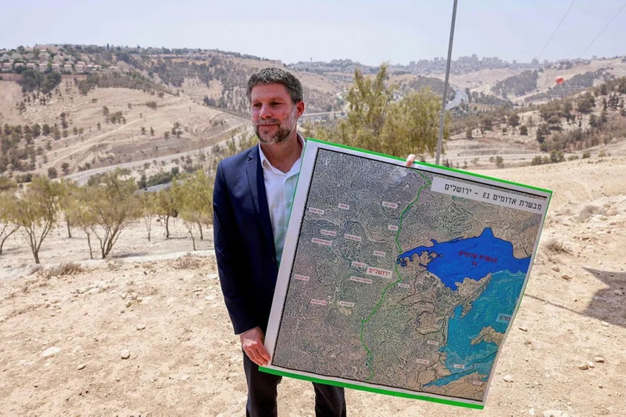 Bezalel Smotrich holding a large map of the E1 area near Jerusalem outdoors.