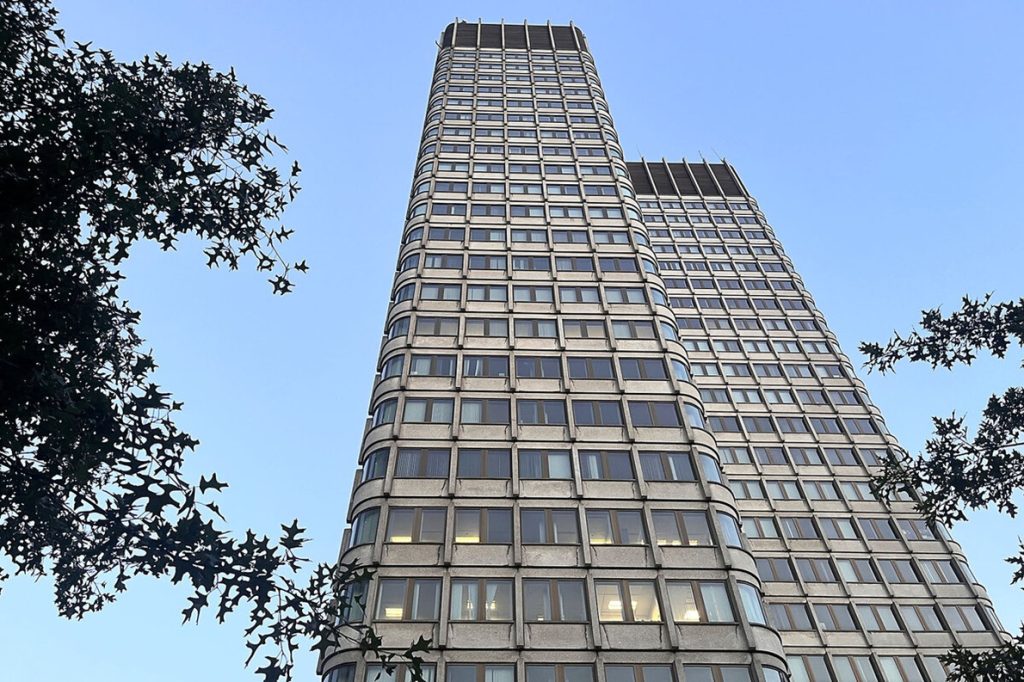 Low-angle view looking up at a tall concrete high-rise building against a clear blue sky.