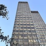 Low-angle view looking up at a tall concrete high-rise building against a clear blue sky.