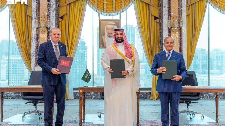 Turkish President Recep Tayyip Erdogan, Saudi Crown Prince Mohammed bin Salman, and Pakistani Prime Minister holding agreement folders indoors.