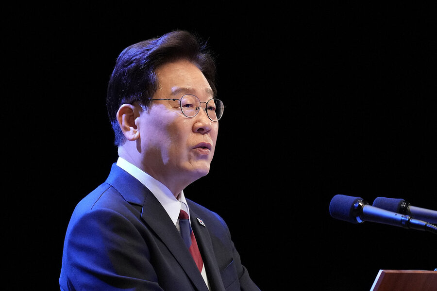 South Korean politician Lee Jae-myung speaking into microphones against a dark background.