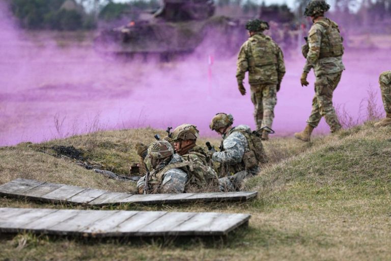 Soldiers in military camouflage gear taking positions in a field during a smoke exercise