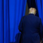 Donald Trump seen from behind walking away through an opening between heavy blue curtains.