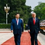Chinese President Xi Jinping and Donald Trump walking down a red carpet past a military honor guard.