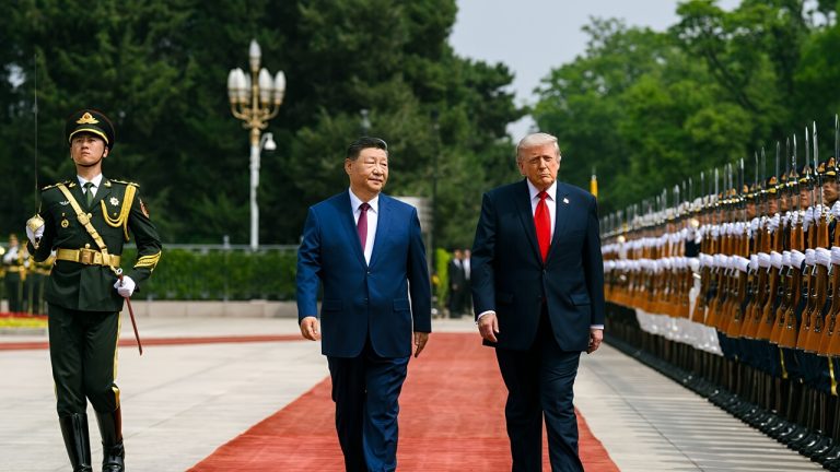 Chinese President Xi Jinping and Donald Trump walking down a red carpet past a military honor guard.