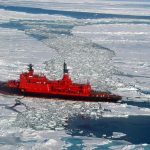 Large red icebreaker ship breaking through frozen Arctic sea ice