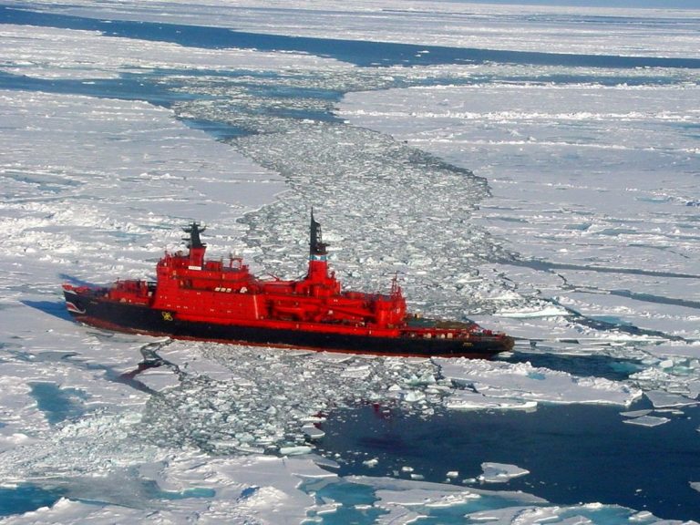 Large red icebreaker ship breaking through frozen Arctic sea ice