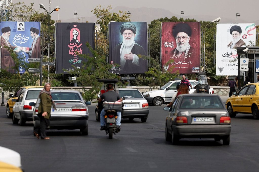 Street traffic in Tehran with large political billboards displaying Ayatollah Ali Khamenei