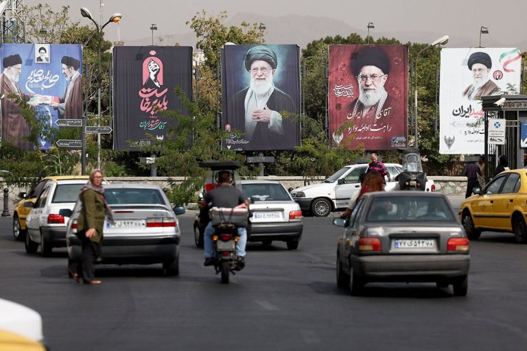 Street traffic in Tehran with large political billboards displaying Ayatollah Ali Khamenei
