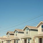 Row of suburban residential homes under a clear blue sky with power lines overhead.