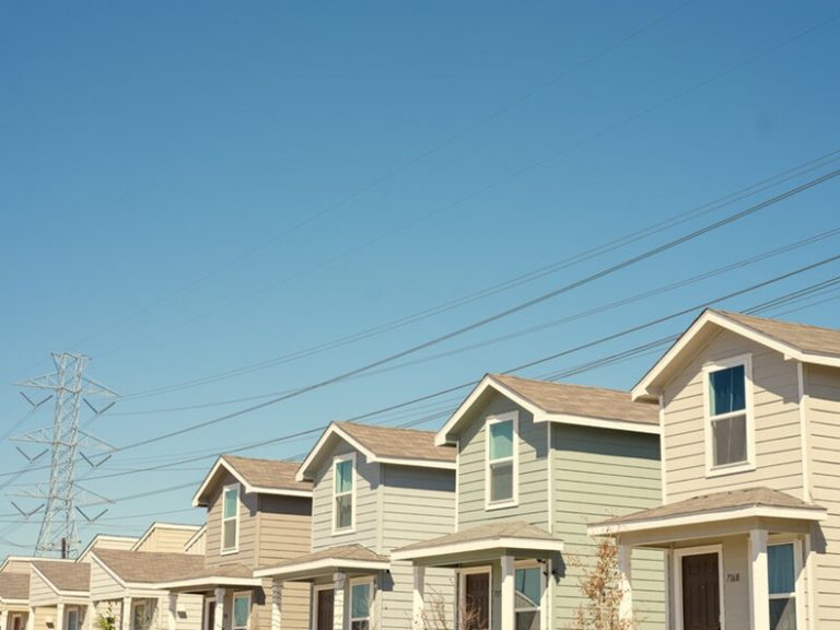 Row of suburban residential homes under a clear blue sky with power lines overhead.