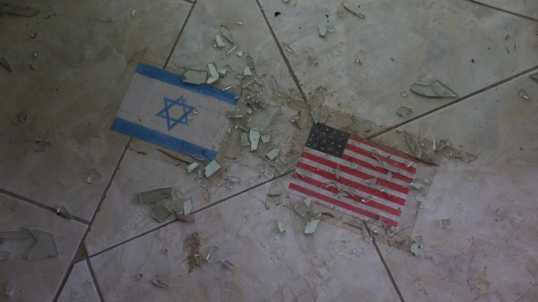 Israeli flag and US flag decals embedded on a tiled floor covered in broken glass shards.