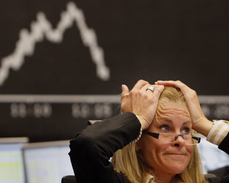 Stressed financial trader holding her head in despair in front of a falling stock market chart.