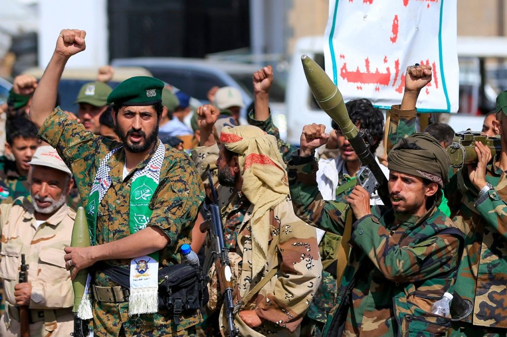 Armed fighters in military attire raising fists and holding weapons during a rally.
