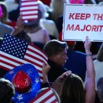 Supporter holding a Keep the Majority sign and American flags in a rally crowd