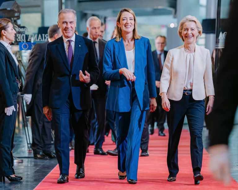 Mark Carney walking alongside European leaders Roberta Metsola and Ursula von der Leyen on a red carpet.