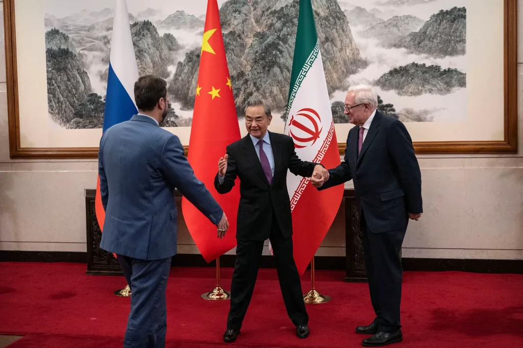 Chinese Foreign Minister Wang Yi standing between Russian and Iranian diplomats with national flags in the background.