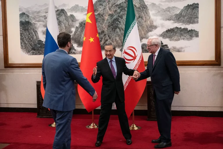 Chinese Foreign Minister Wang Yi standing between Russian and Iranian diplomats with national flags in the background.