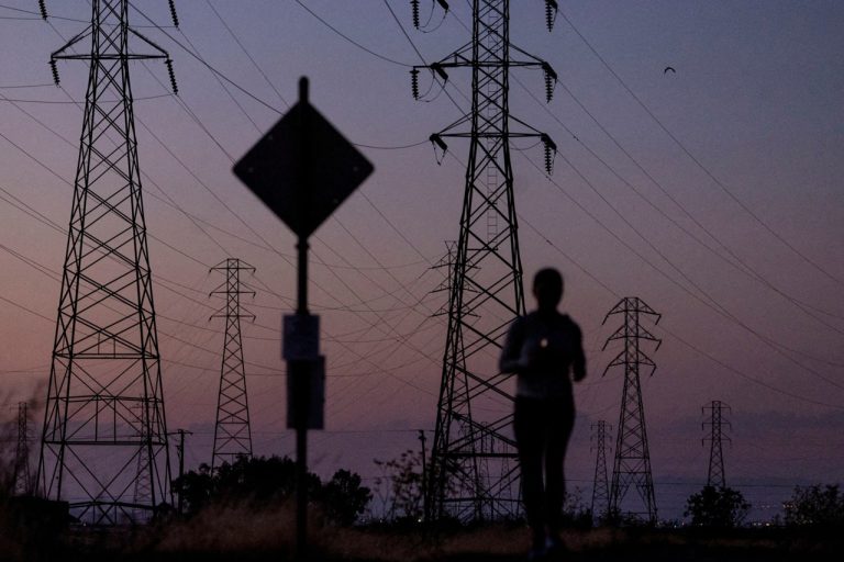 Silhouette of high-voltage power line towers against a twilight sky with a person jogging.